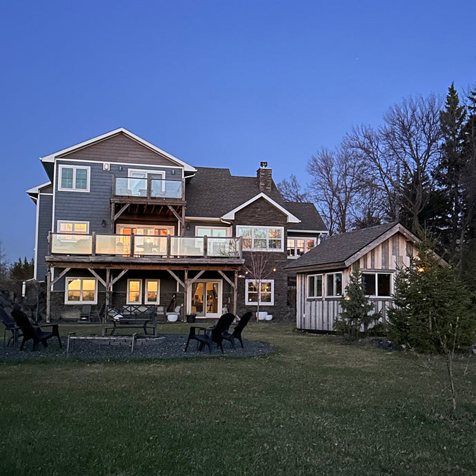 Large two-story house with a dark roof and light walls, surrounded by trees and grass.