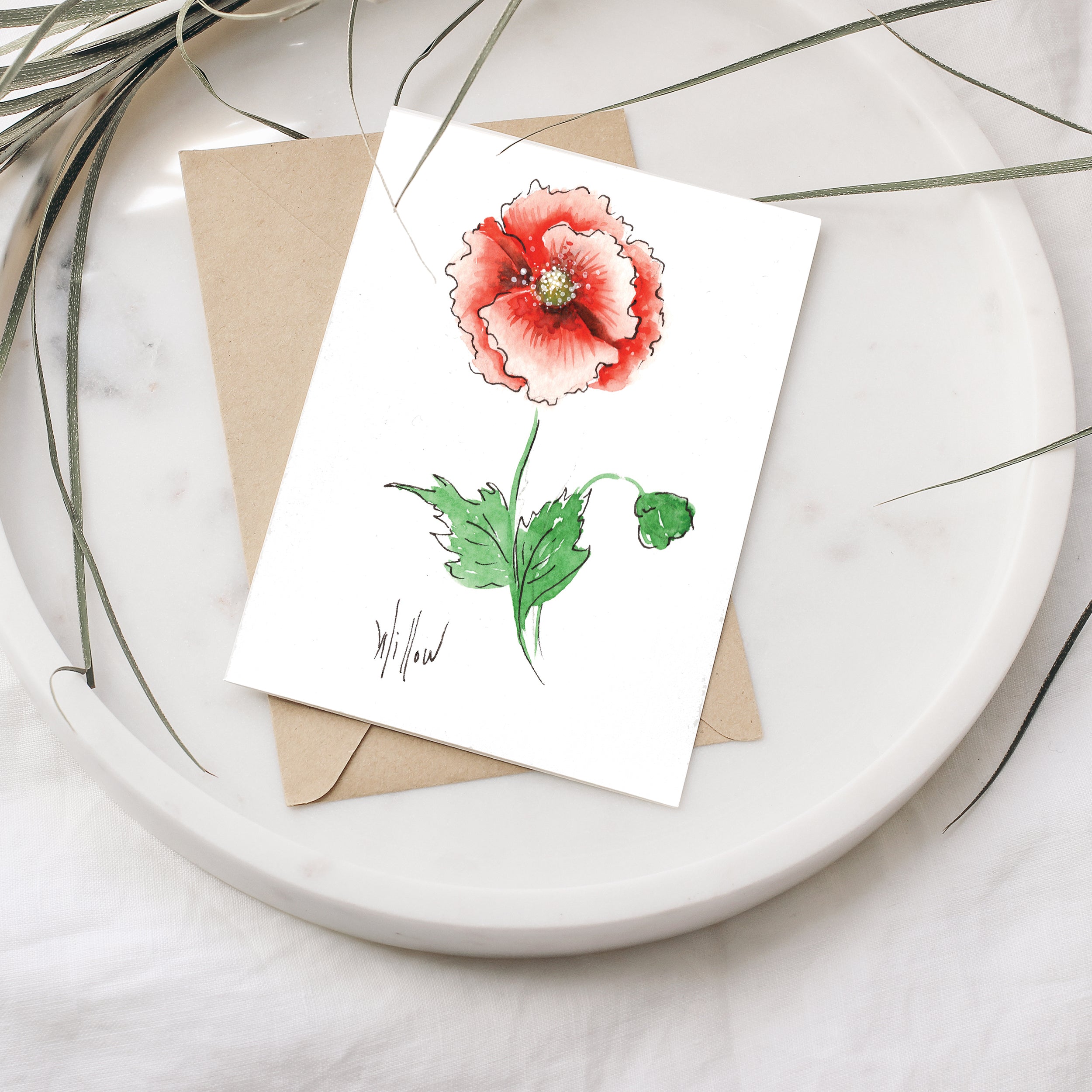 Greeting card with a red flower illustration on a white plate with a brown envelope.