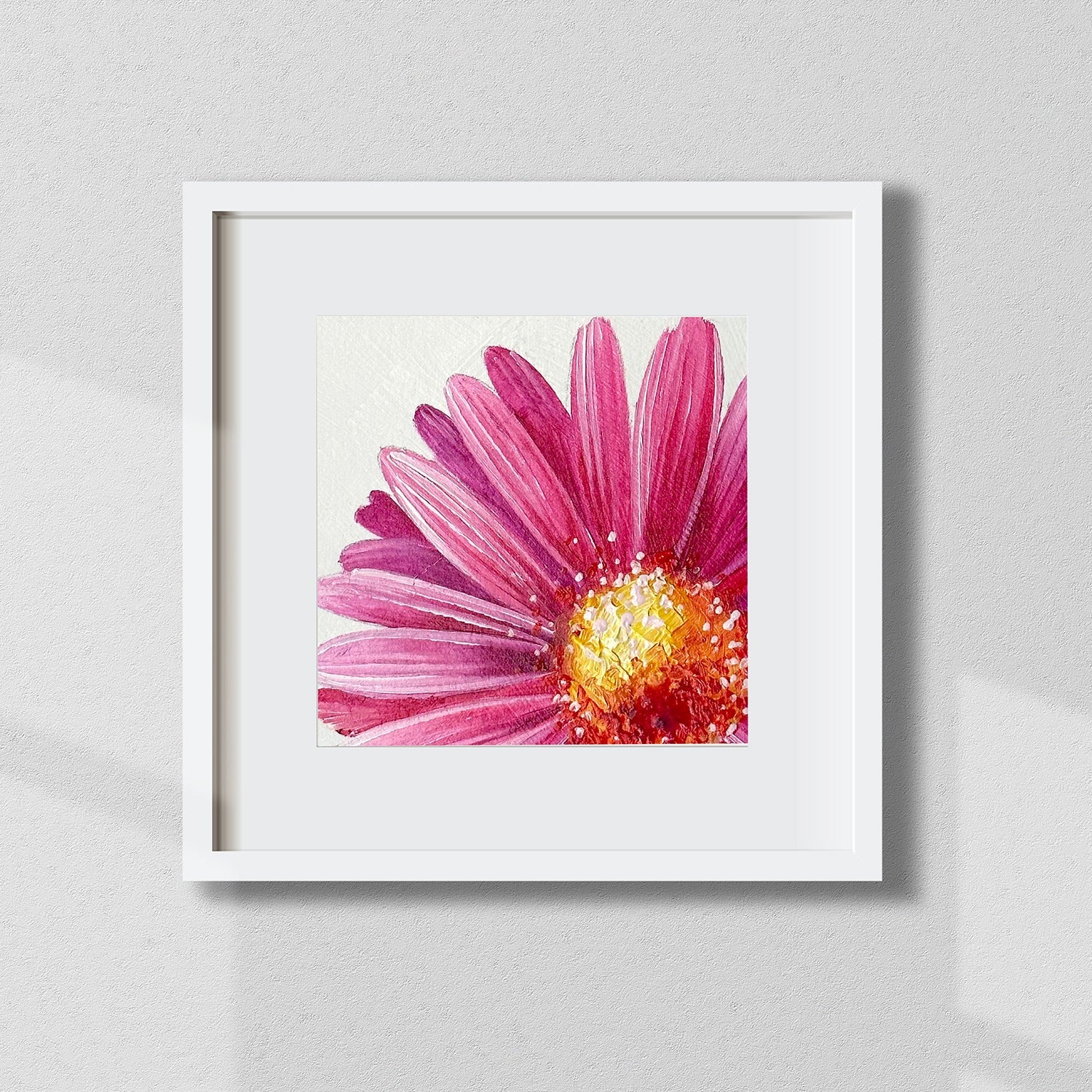 Framed artwork of a pink flower with a white border on a light gray wall.
