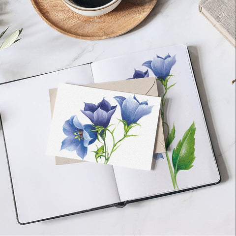 Open notebook with blue floral illustration, cup of coffee on wooden coaster