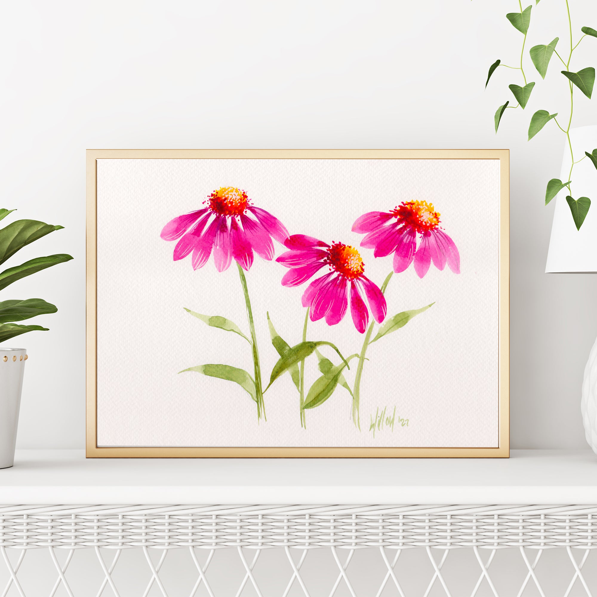 Framed artwork of pink flowers on a white wall with plants around