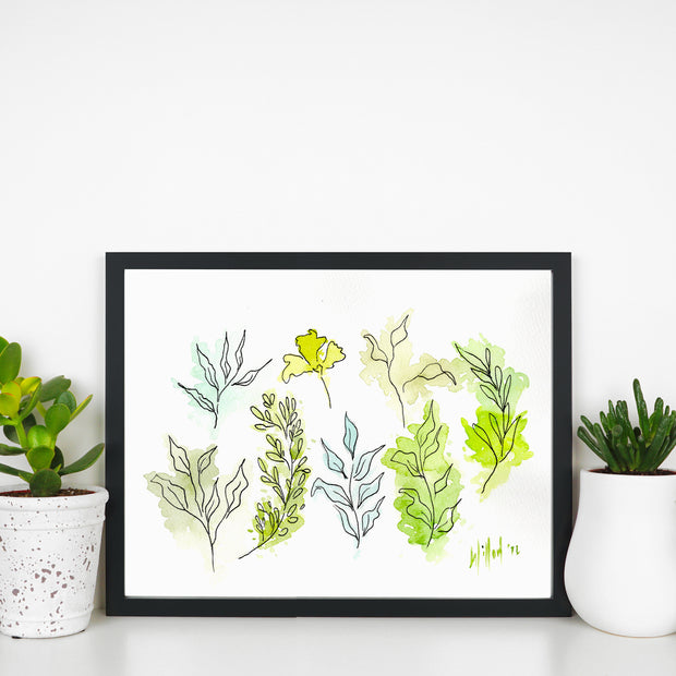 Framed artwork with green leaf patterns on a white surface with plants.