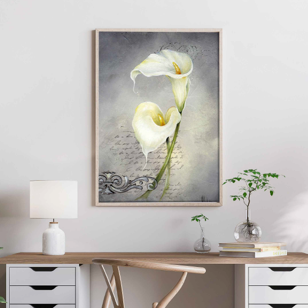 Framed artwork of calla lilies above a desk with a lamp and plant.