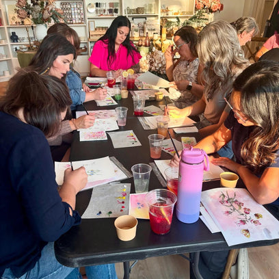 Group of people sitting around a table engaged in an activity, possibly a craft or painting session.